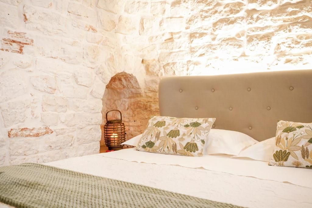 Quarto com parede de tijolos brancos, cama com cabeceira cinza e um candeeiro numa mesa de cabeceira.