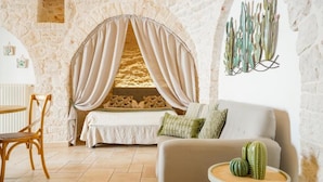 A cozy room with a stone wall, a bed with a canopy, a sofa, a small table with a cactus, and a wall-mounted cactus decoration. - Trulli Di Zia Vittoria (Alberobello)