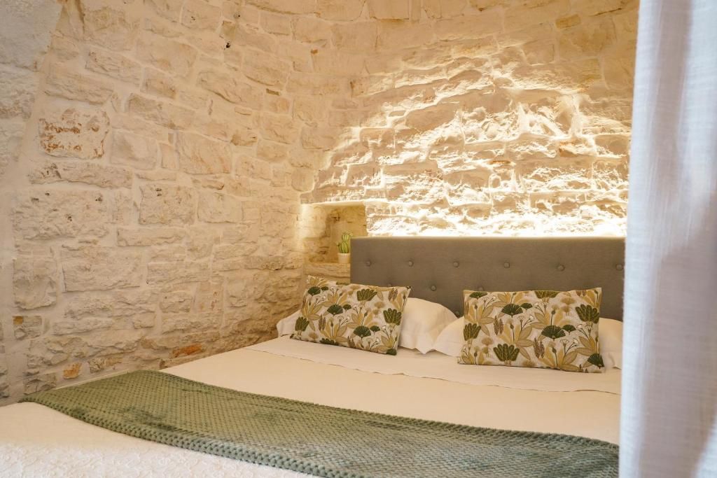 A bedroom with a stone wall, a bed with floral pillows, and a green blanket.