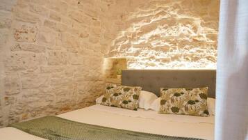 A bedroom with a stone wall, a bed with floral pillows, and a green blanket.