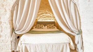 A bed with a canopy, a stone wall, and a headboard. - Trulli Di Zia Vittoria (Alberobello)