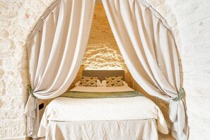 A bed with a canopy, a stone wall, and a headboard. - Trulli Di Zia Vittoria (Alberobello)