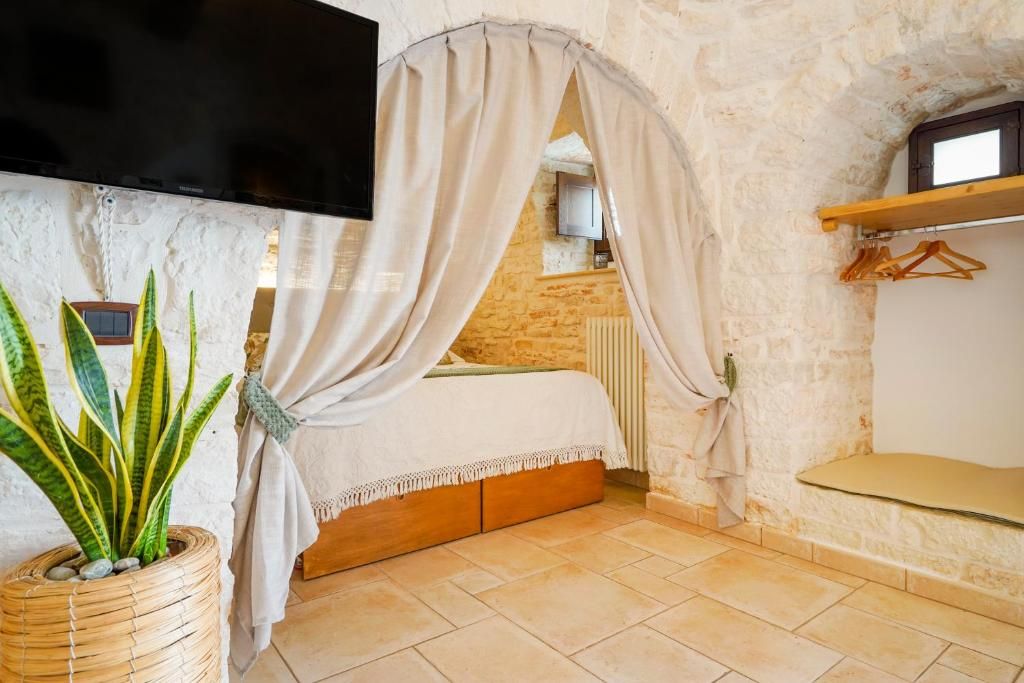 Una camera da letto con un letto, una televisione a muro, una pianta in vaso e un muro in pietra.