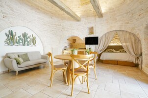 Una stanza accogliente con una parete in pietra, un tavolo da pranzo in legno con sedie, un divano, una TV a parete e un letto a baldacchino.
