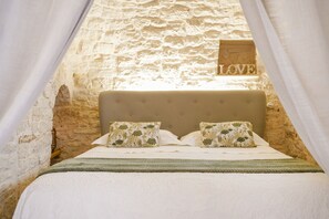 A bedroom with a stone wall, a bed with floral pillows, and a 'LOVE' sign above the bed. - Trulli Di Zia Vittoria (Alberobello)