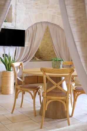 A dining area with a round table and four chairs, a potted plant, and a television mounted on the wall.