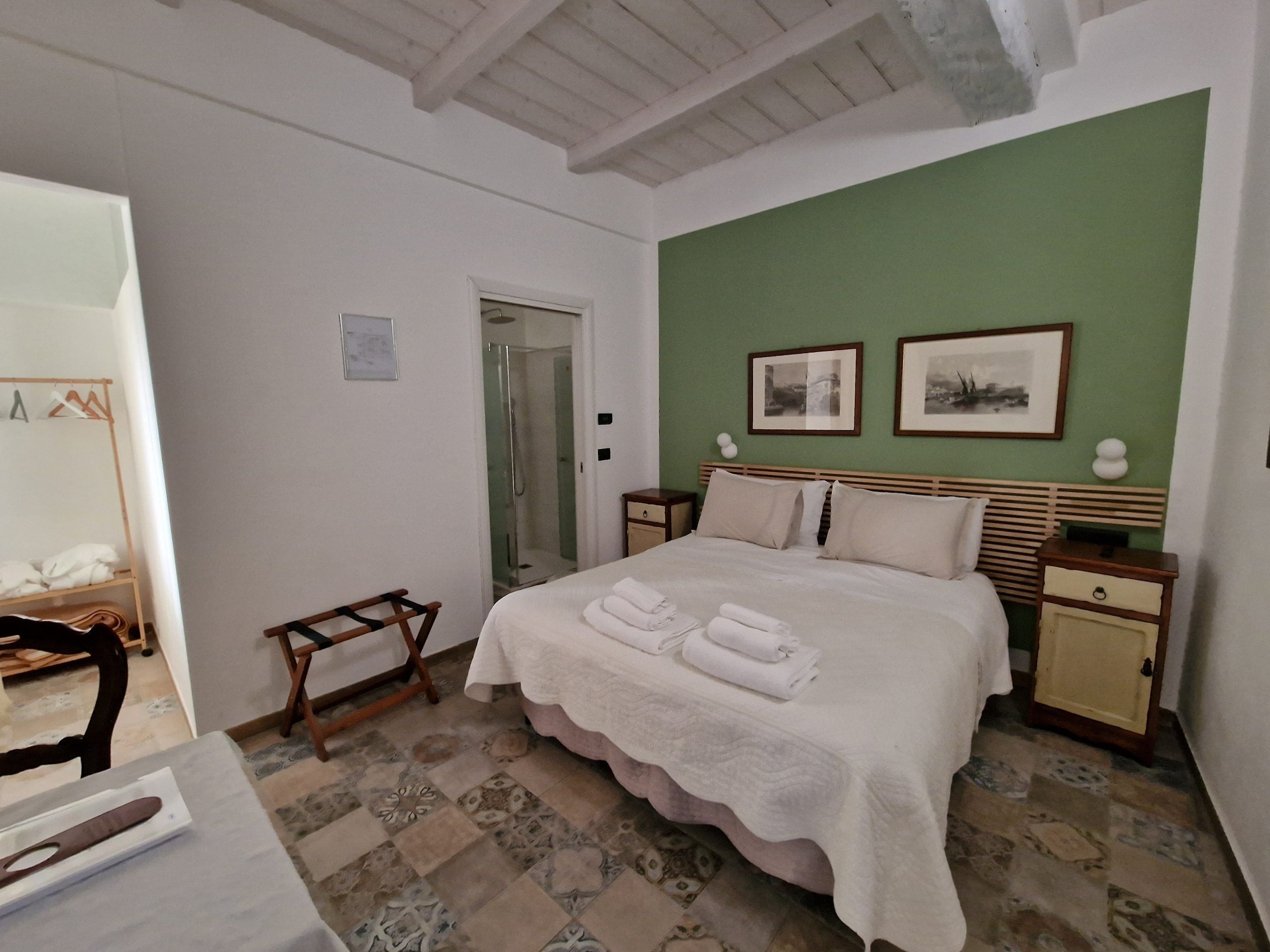 Ein Schlafzimmer mit einem Bett, zwei Nachttischen, einem kleinen Tisch, einem Holzstuhl, einem Spiegel und einer Dusche.