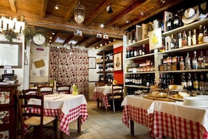 Interior de un restaurante con vigas de madera, manteles a cuadros y estantes llenos de botellas.