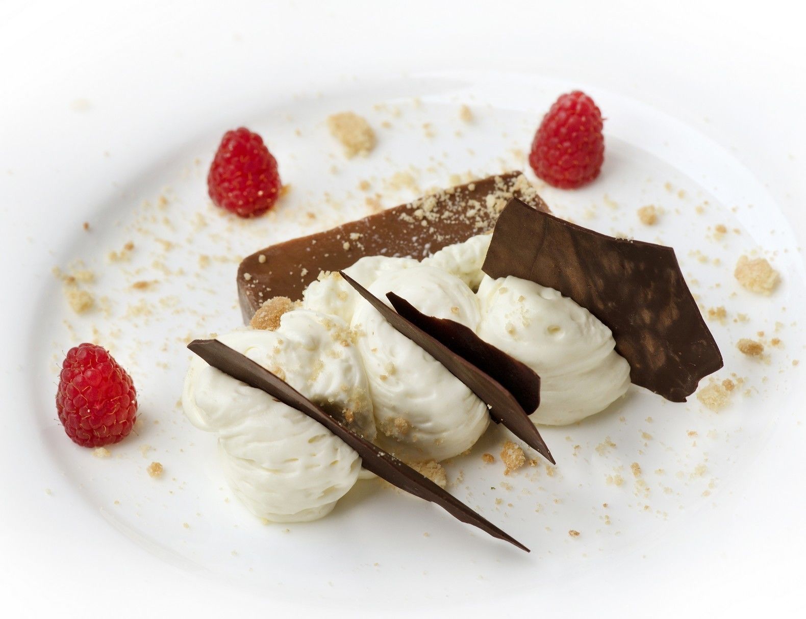 Un dessert composé de crème blanche, de morceaux de chocolat et de framboises, présenté dans une assiette.