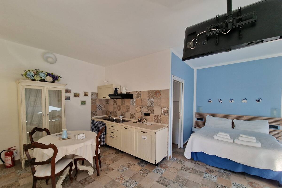 A compact bedroom with a bed, a small kitchenette, and a dining area with a table and chairs.