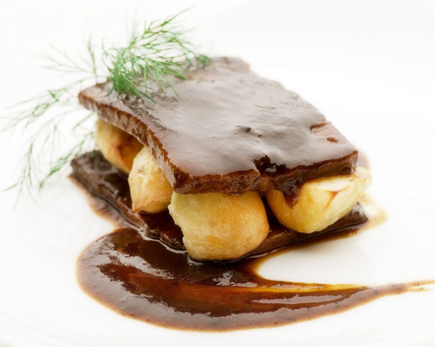 A dessert with a chocolate glaze, bananas, and a sprig of dill on a white plate.