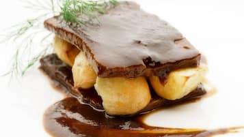 A dessert with a chocolate glaze, bananas, and a sprig of dill on a white plate.