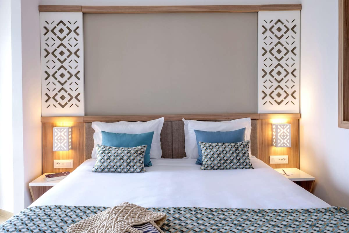 A neatly made bed with two pillows, a patterned throw blanket, and two bedside lamps.