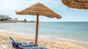 A beach with a straw umbrella, a lounge chair, and a beach chair.