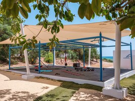 An outdoor gym with exercise equipment, a shaded area, and a view of the sea.