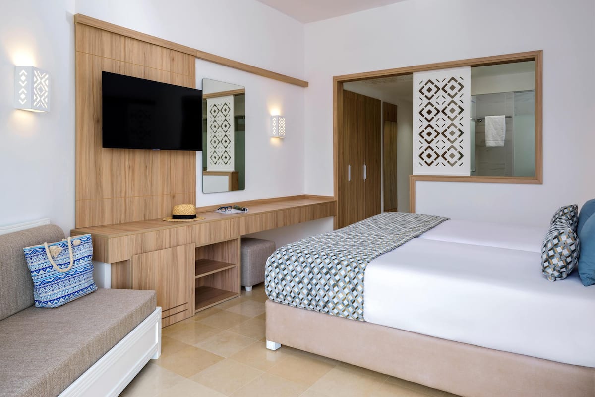 A modern bedroom with a bed, a TV mounted on a wooden panel, a desk with a chair, and a wardrobe.