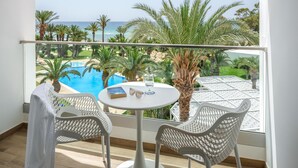 A balcony with a view of a pool and palm trees, featuring two white chairs and a small table with a book and glasses.