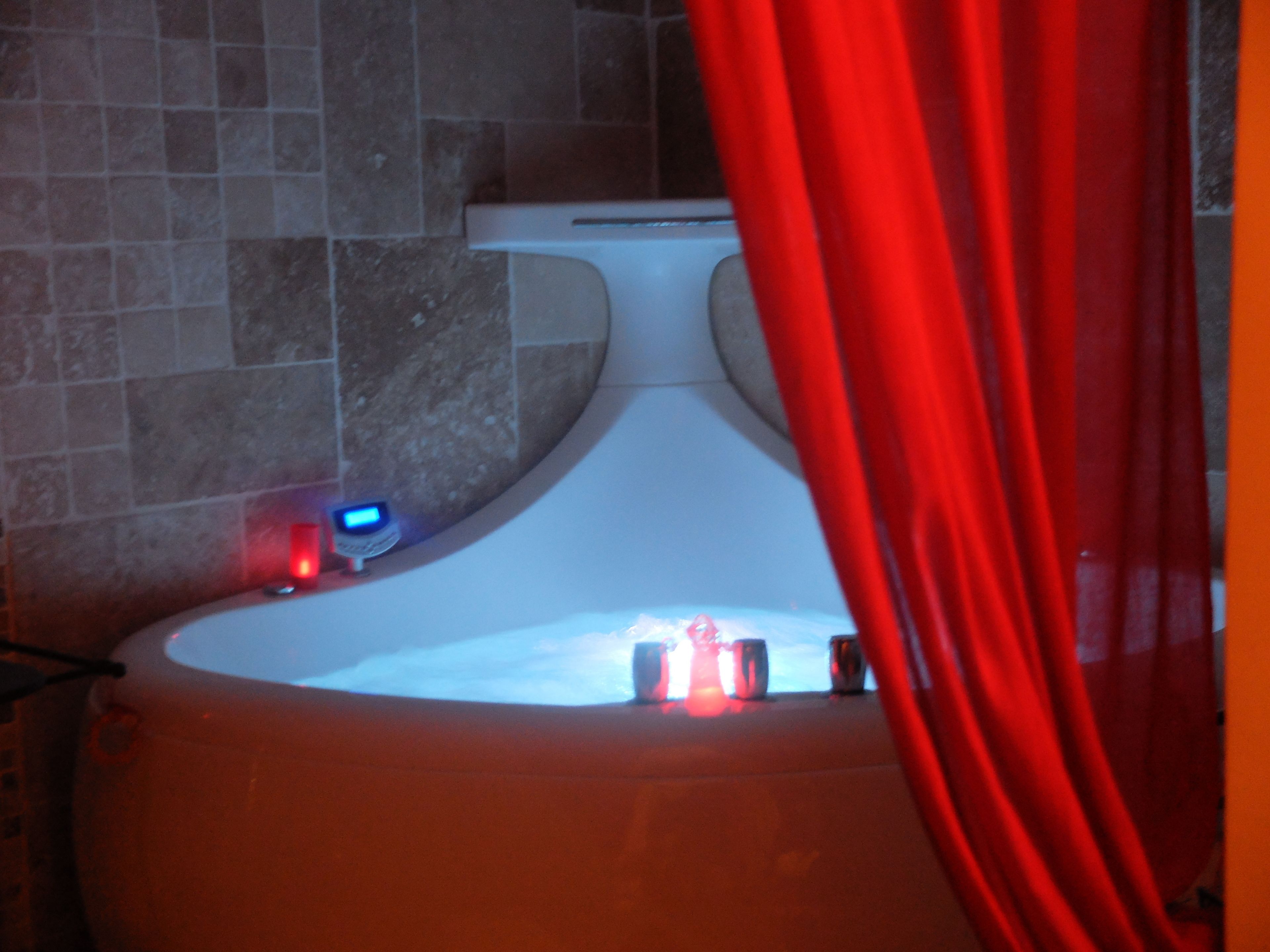 A bathroom with a bathtub, a red curtain, and a digital clock on the wall.