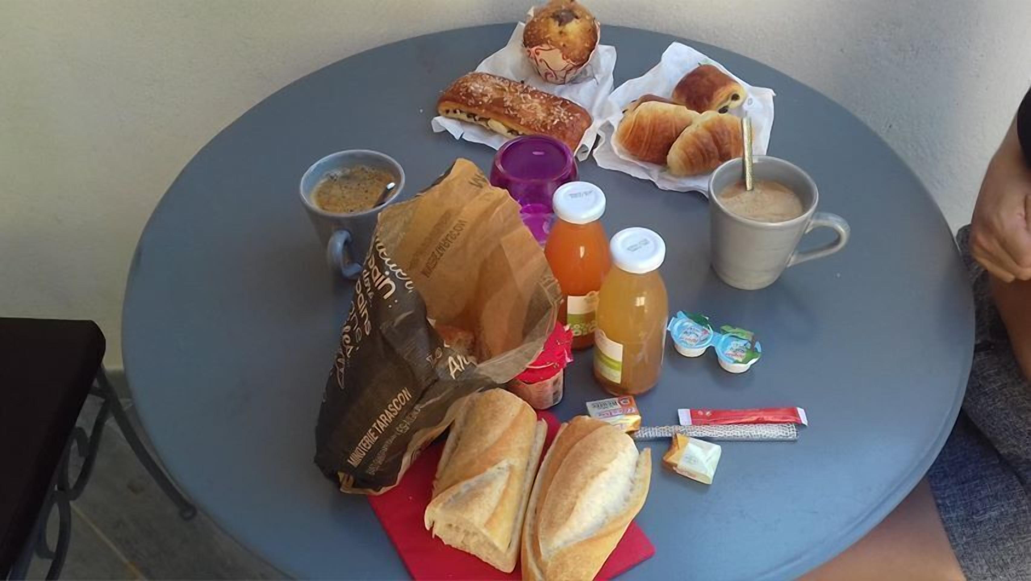 A round table with a variety of food items including pastries, a coffee mug, a juice bottle, and a bag of snacks.
