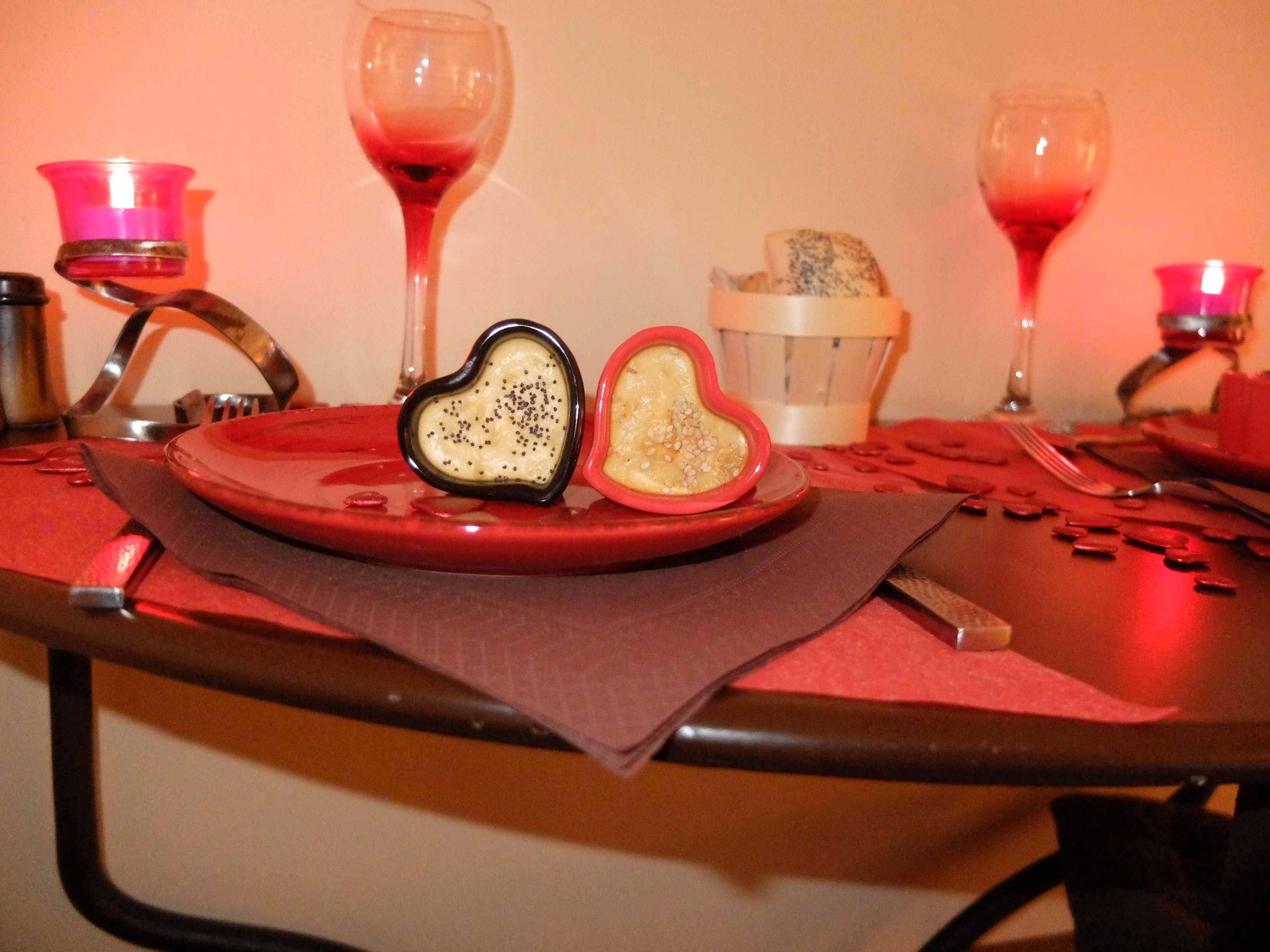 A table set with a red plate, heart-shaped bowls, and wine glasses.