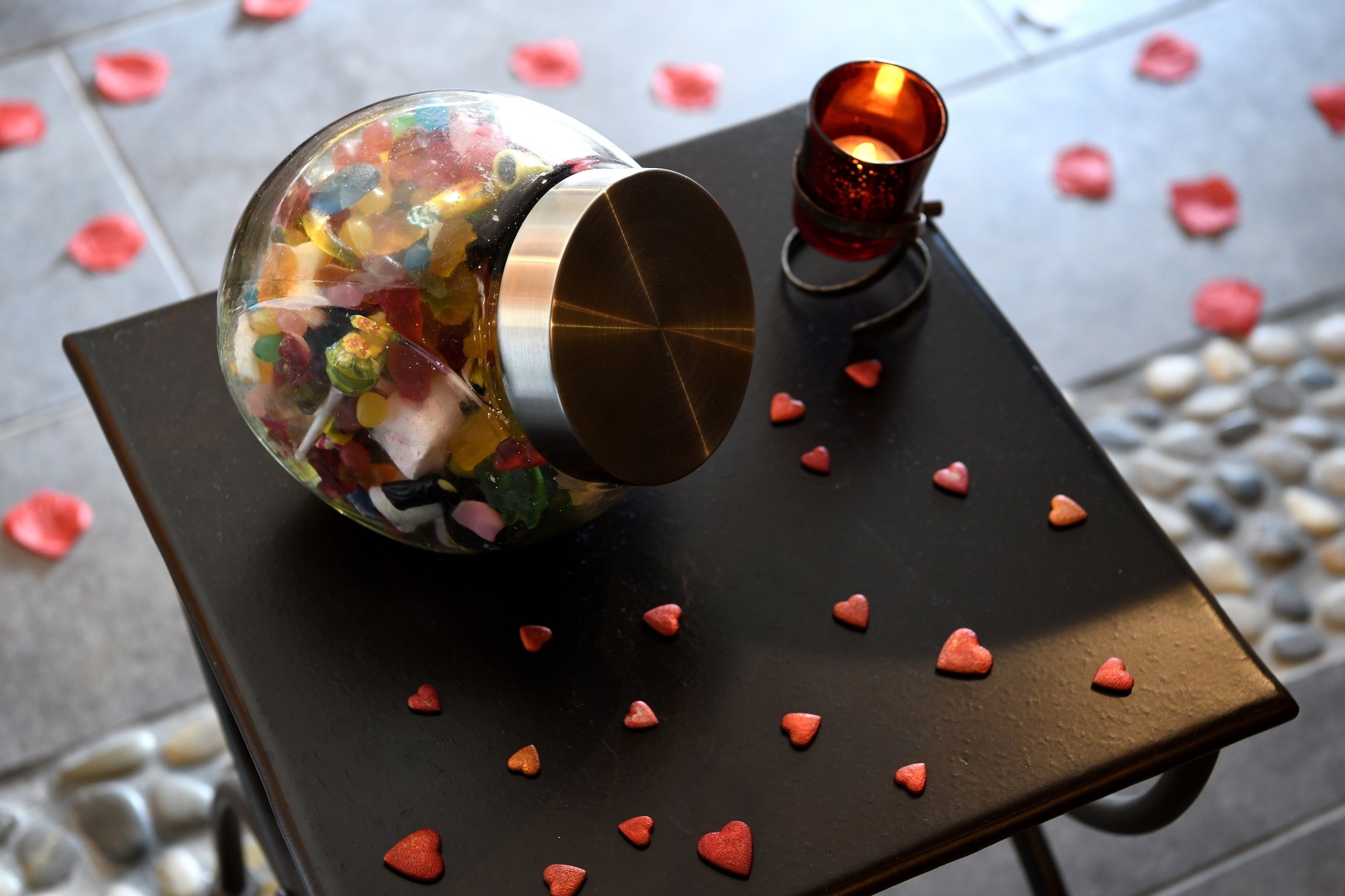 A glass jar filled with colorful candies on a table with a candle and heart-shaped decorations.