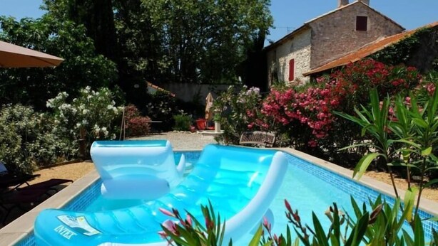 Una piscina con tumbonas hinchables, rodeada de exuberante vegetación y un edificio de piedra.
