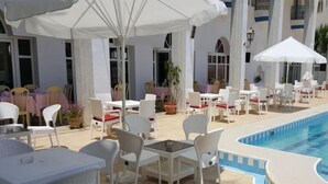 Zona junto a la piscina con mobiliario exterior blanco, incluyendo mesas y sillas, y sombrillas que dan sombra.