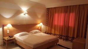 Habitación de hotel con cama doble, dos lámparas de noche, mesita de noche con teléfono y cortina de estampado cruzado.