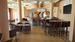Un vestíbulo de hotel con zona de bar, arreglos de asientos y un televisor montado en la pared.