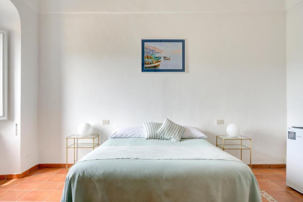 A bedroom with a bed, two bedside tables, a wall-mounted painting, and a white wardrobe.