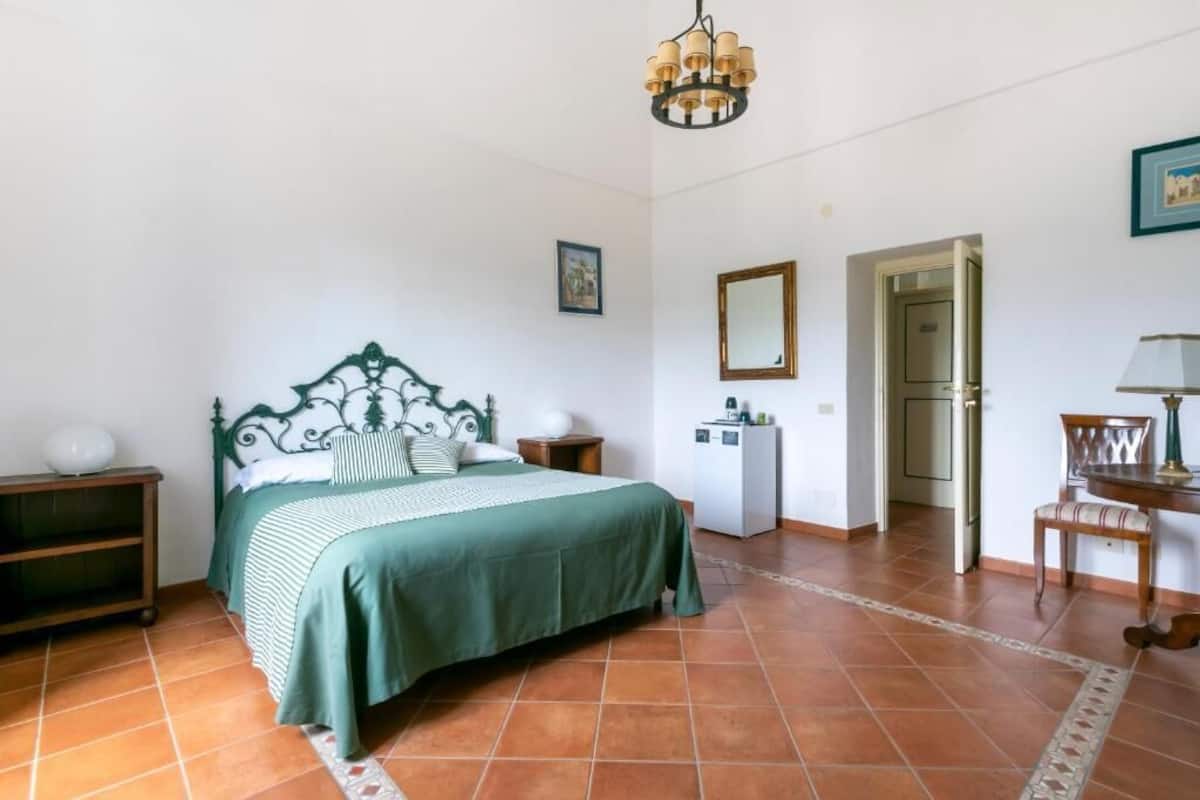Een slaapkamer met een bed, nachtkastjes, een bureau, een stoel, een spiegel en een deur.