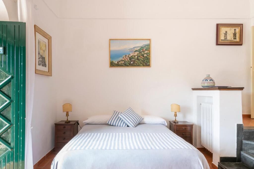 A bedroom with a bed, two bedside tables with lamps, a radiator, and a painting on the wall.