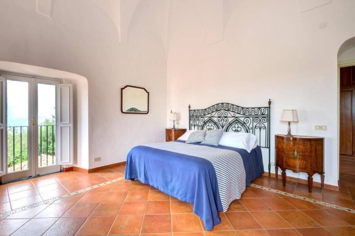 Een slaapkamer met een bed, twee nachtkastjes, een spiegel en een uitzicht door een deur.