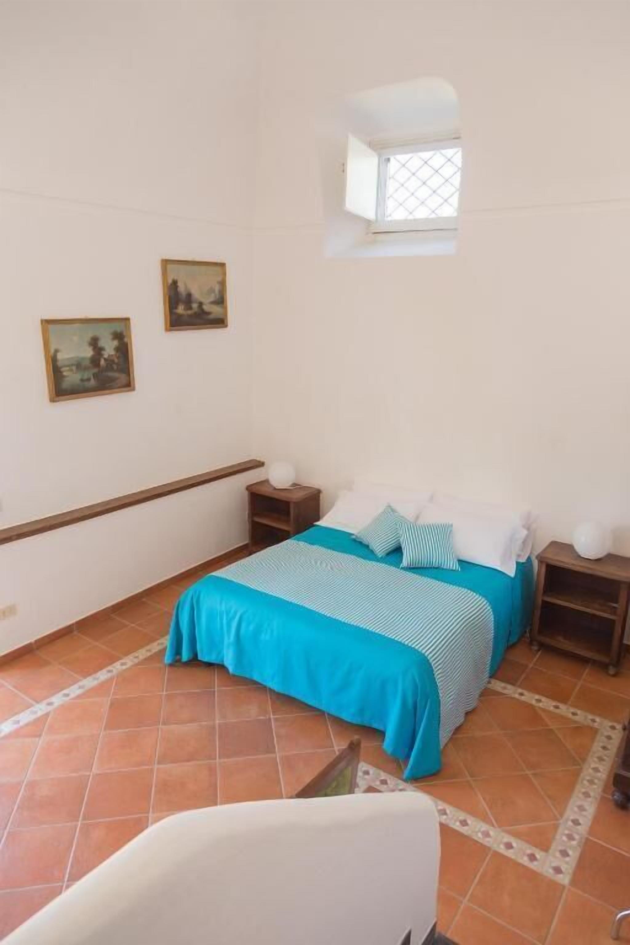 Ein Schlafzimmer mit einem Bett, Nachttischen, einem Fenster und zwei Wandbildern.