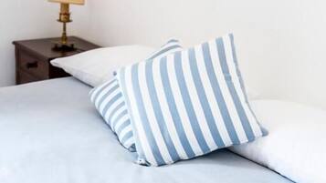 Un letto con un cuscino a righe e un cuscino semplice, un comodino con una lampada, e una parete neutra.