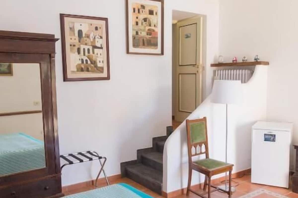 Een slaapkamer met een bed, een stoel, een klein tafeltje, een radiator en een trap.