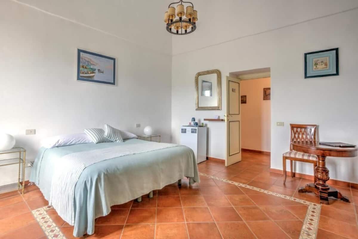 Een slaapkamer met een bed, nachtkastje, kaptafel en een klein bureau met stoel.