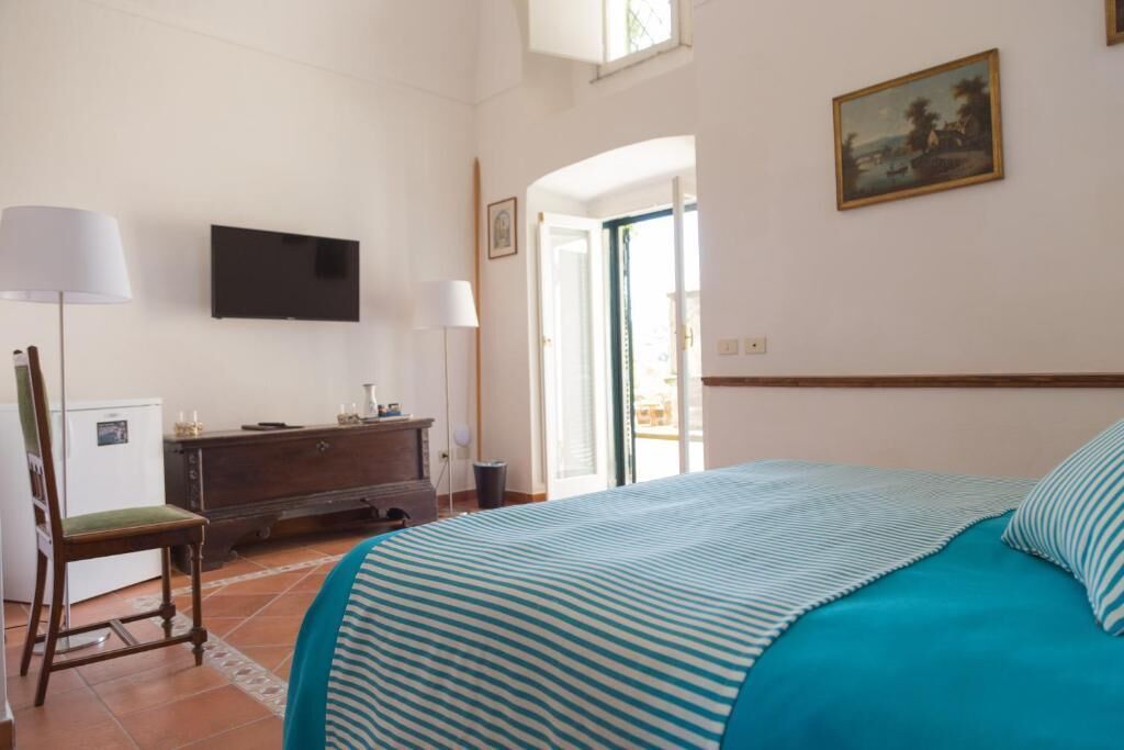 Un dormitorio con cama, cómoda, televisor y puerta que da a un balcón.