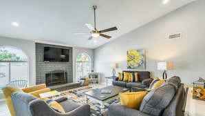 A modern living room with a fireplace, grey sofas, yellow cushions, and a large window. - Pool & Putting Green: Scottsdale Family Escape (Scottsdale)