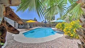 A swimming pool surrounded by pebbles, palm trees, and yellow flowers. - Pool & Putting Green: Scottsdale Family Escape (Scottsdale)