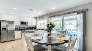 A modern kitchen with white cabinets, stainless steel appliances, and a dining area with a wooden table and chairs. - Pool & Putting Green: Scottsdale Family Escape (Scottsdale)