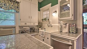 Una cocina con armarios blancos, encimera de granito, un lavabo y una cafetera.