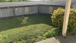 Blick auf einen Garten mit einer Holzterrasse, einem Rasen und einem Gewässer im Hintergrund.