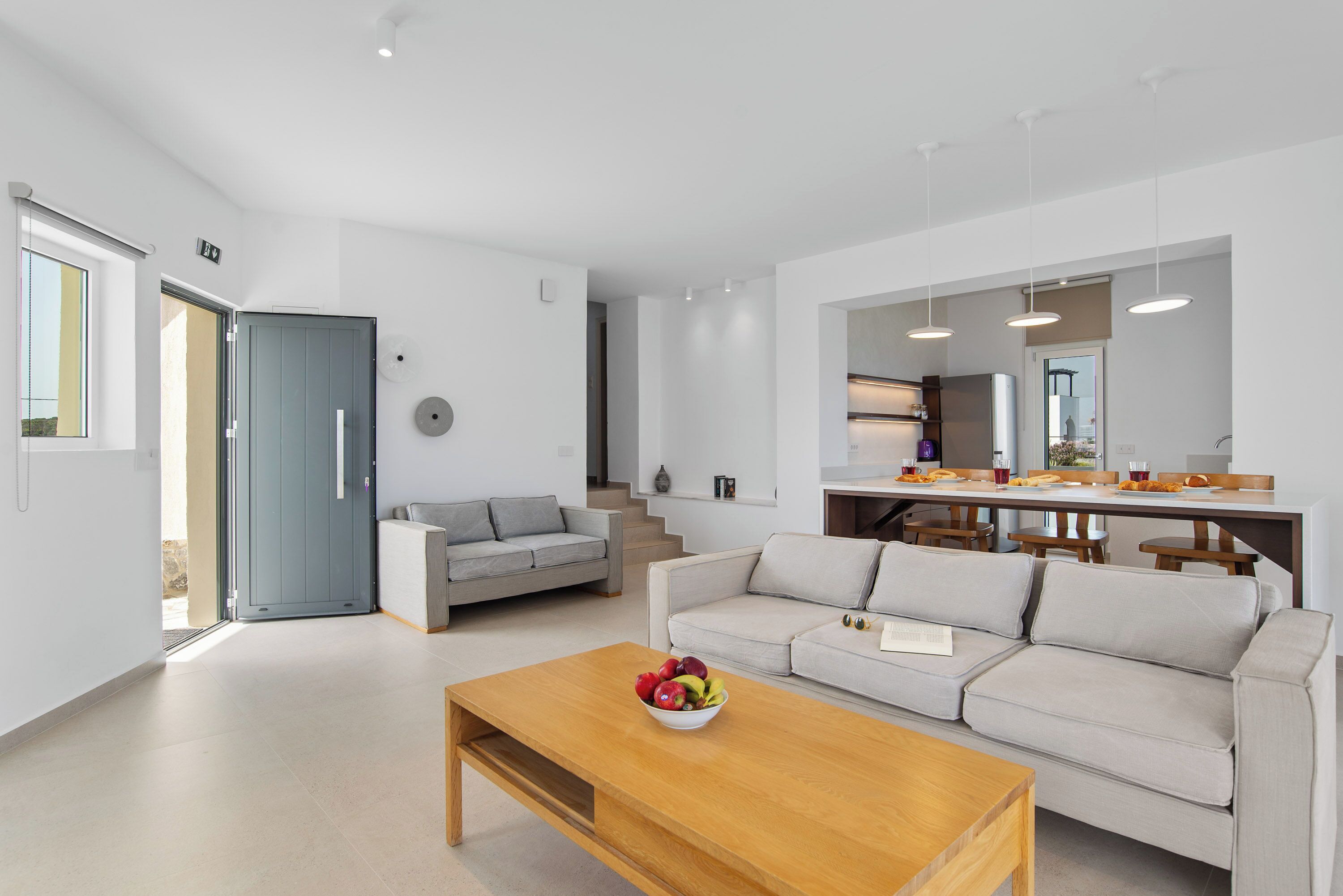 Een moderne woonkamer met een bank, salontafel en een eethoek met stoelen en een keukenwerkblad.