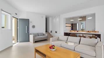Een moderne woonkamer met een bank, salontafel en een eethoek met stoelen en een keukenwerkblad.
