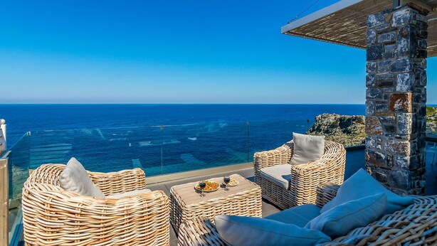A balcony with wicker furniture, a stone wall, and a view of the ocean.