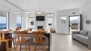 A modern kitchen with a dining area, large windows, and a view of the sea.