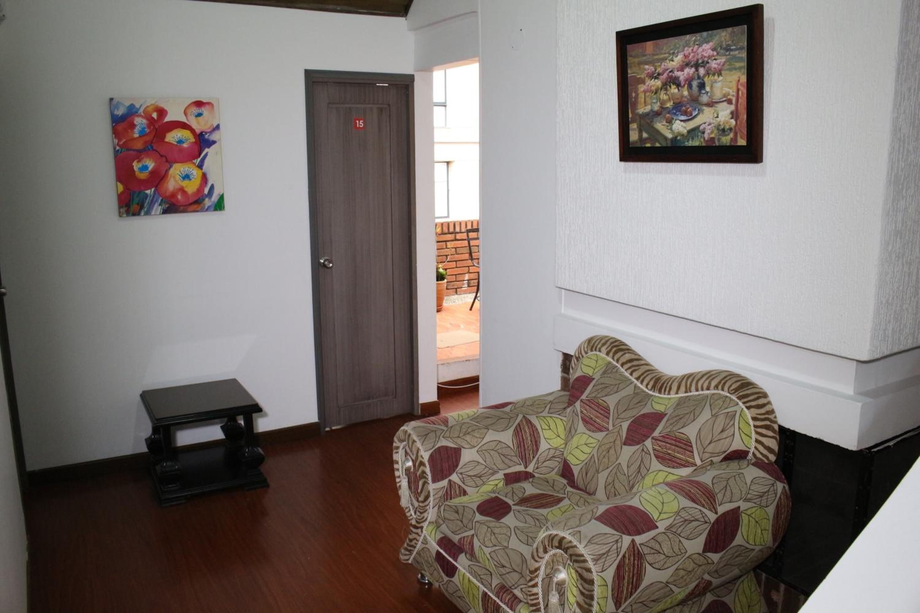 A room with a patterned sofa, a small table, a door, and two paintings on the walls.
