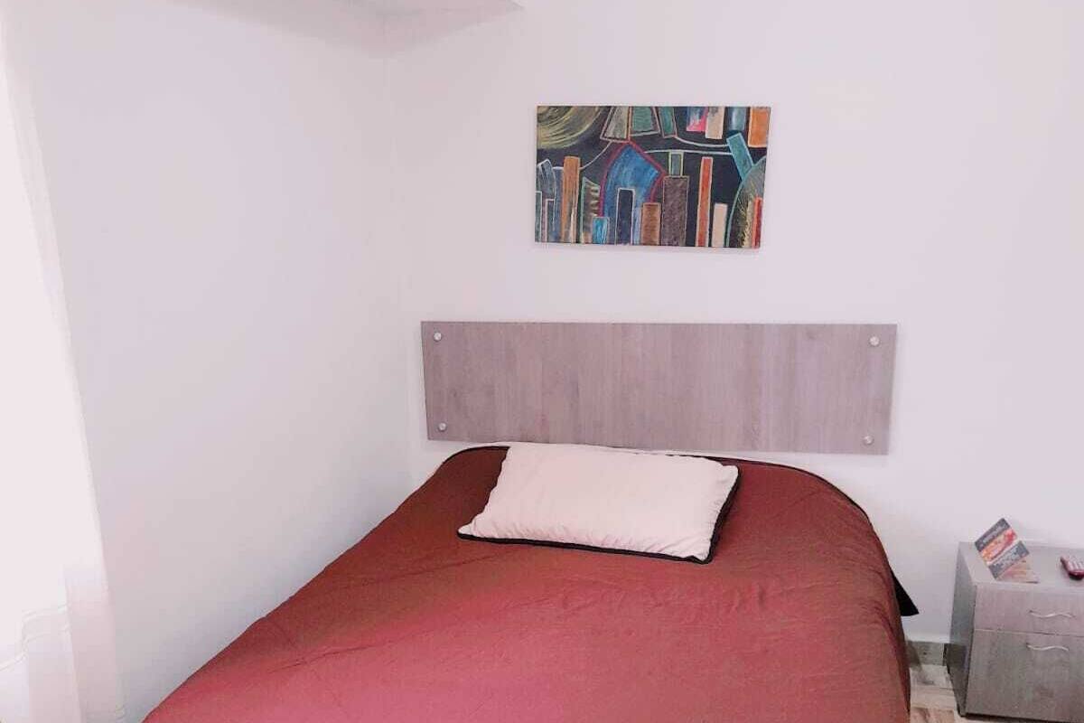 A bedroom with a wooden headboard, a red bedspread, and a painting above the bed.