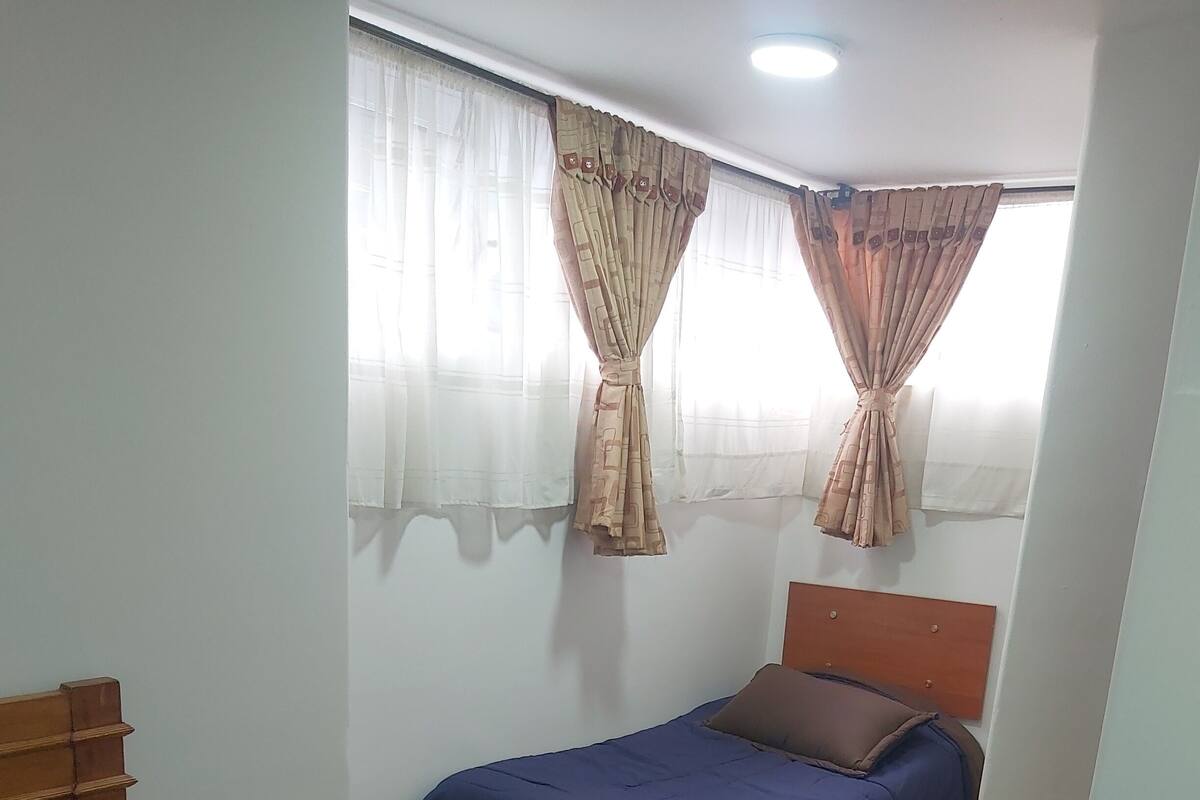 A room with two beds, a wooden headboard, a small wooden cabinet, and a remote control on the floor.